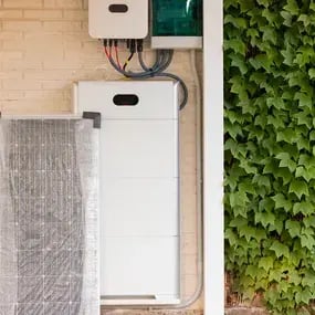Solarpanel und Batteriespeicher neben einer begrünten Wand an einer Ziegelmauer