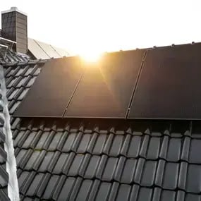Sonnenstrahlen treffen auf schwarze Solarpanels auf einem Ziegeldach