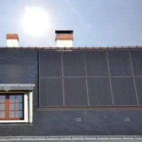 Solarpaneele auf einem Schieferdach bei Sonnenschein, daneben ein gemauerter Schornstein