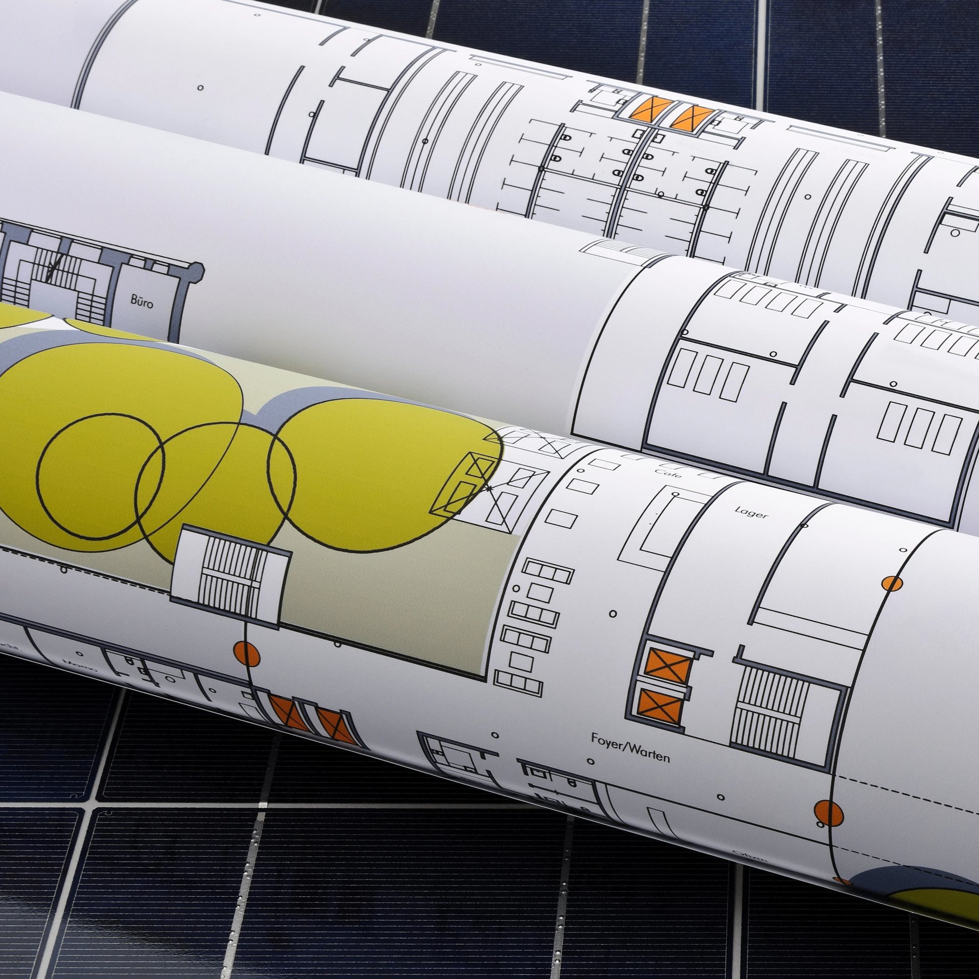 Gerollte Baupläne zur Photovoltaik-Planung auf einem Solarpanel im Hintergrund